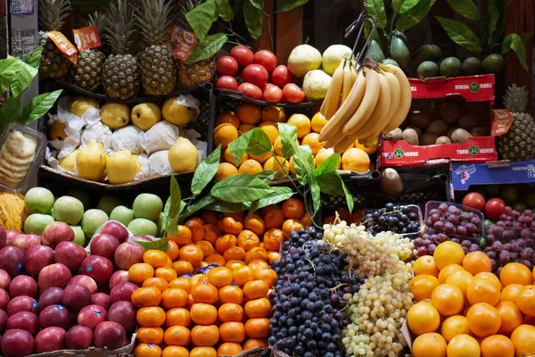 Manavın önünde farklı meyve çeşitleri var.