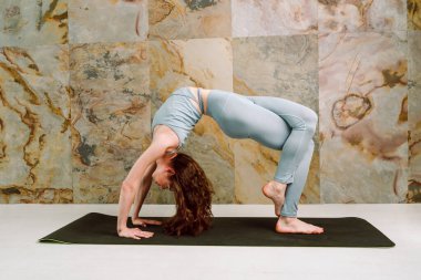 Genç yogini, Chakrasana 'nın değişik pozlarını uyguluyor. Pastel mavi tozlar ve üst, seçici odak noktası.