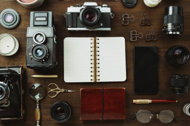 Klasik film kamerası, lensler ve kırsal düzlükteki siyah ahşap masa üzerindeki kırtasiye malzemesi.