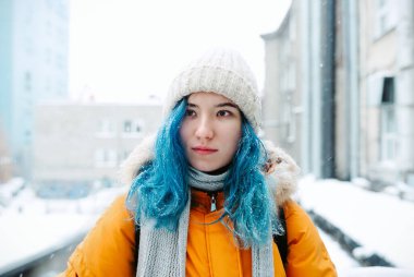 Beyaz örgü şapkalı boyalı, kar yağışı altında duran, seçici odaklı Asyalı genç bir kadın.