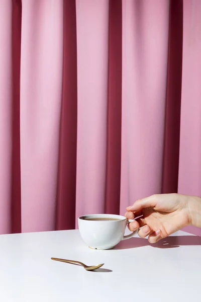 ピンクのドレープの前に白いテーブルの上にお茶やコーヒーの女性の手を保持カップ 選択的な焦点 — ストック写真