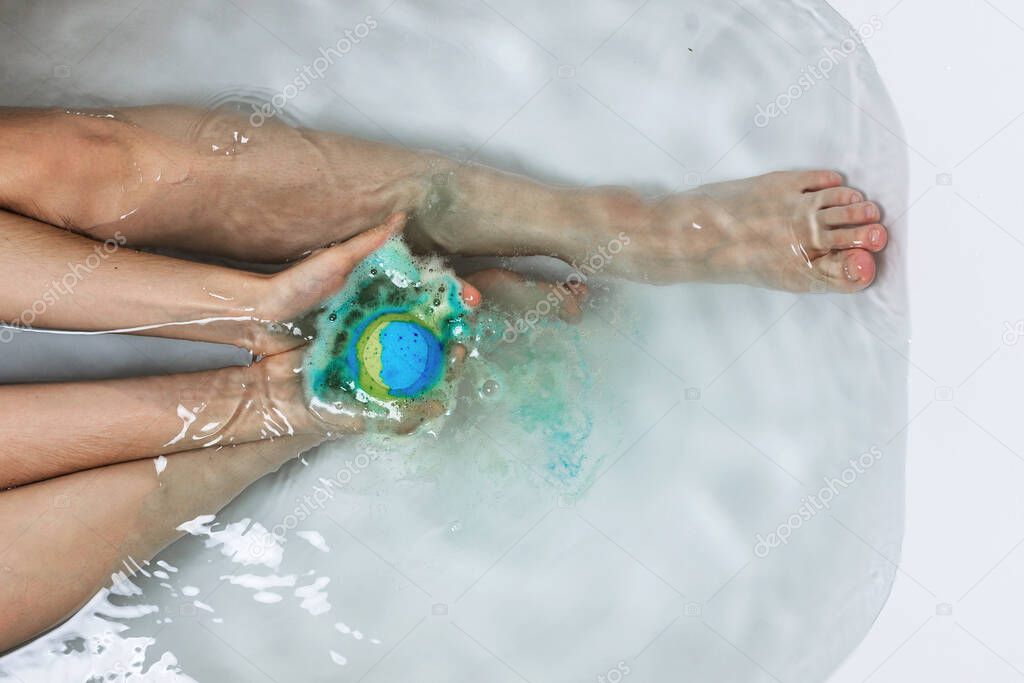 Above shot of woman's legs and hands holding bath bomb in a tub, bodypositive of self care concept