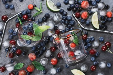 Koyu arkaplanda buzlu soda, eko metal pipetler, nane, şifalı otlar, böğürtlen, buz ve dumanlı iki bardak, seçici odaklanma