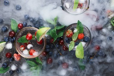 Koyu arkaplanda buzlu soda, naneli, otlu, böğürtlenli, buzlu ve dumanlı, seçici odaklı üç bardak.