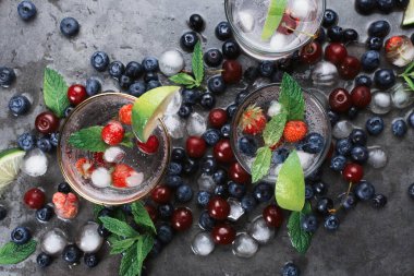 Koyu arkaplanda buzlu soda, eko metal pipetler, nane, şifalı otlar, böğürtlen, buz ve dumanlı iki bardak, seçici odaklanma