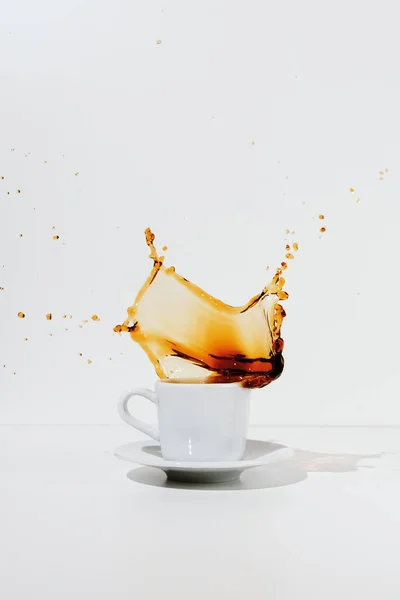 White cup and saucer with splashing coffee, selective focus