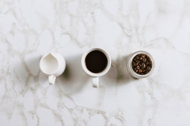 Bitkisel sütlü krema, bir fincan kahve ve mermer fasulyeli kavanoz