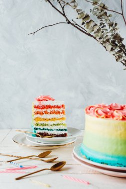 Bir parça vejetaryen gökkuşağı pastası ve beyaz ahşap bir masada doğum günü mumları seçici bir odak noktası.