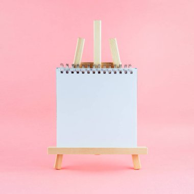 Pembe arkaplan üzerine boş sayfa çizim defteriyle ahşap sehpa çiziliyor, kare resim