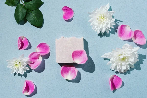Flatlay of natural handmade soap with flowers and petals on blue backgound