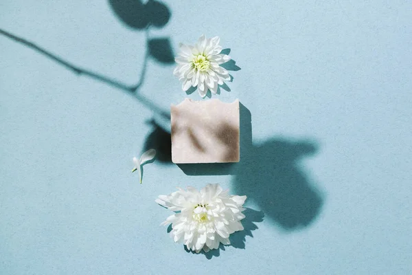 Minimalist flatlay of natural handmade soap with flowers and petals on blue backgound, selective focus