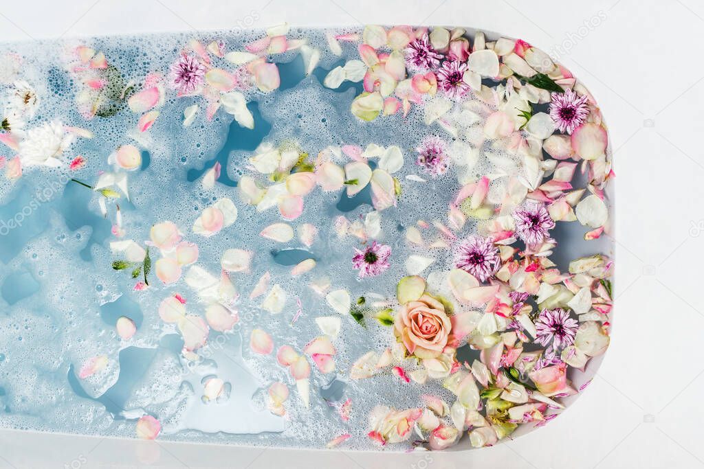 Top view of bath filled with blue bubble water, flowers and petals, spa or selfcare concept