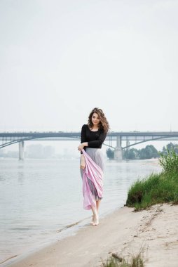 Genç bir kadın elinde pembe bir eşarpla sahilde yürüyor.