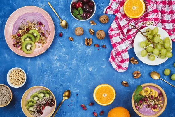 Flatlay with healthy vegan breakfast of berry plant-based yogurt bowls with granola, chia seeds, various fruits and nuts on blue background with copyspace — Stock Image Flatlay Healthy Vegan Breakfast Berry Plant Based Yogurt Bowls Granola Stock Photo