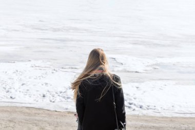 Donmuş nehrin önünde duran sarı saçlı, seçici odaklı genç kadının arkasında.