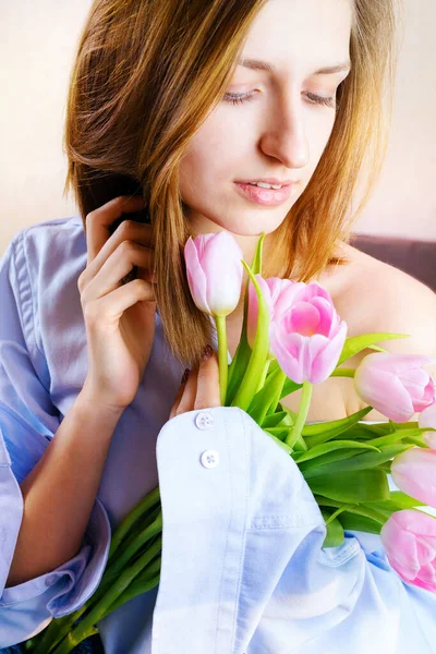 Portrait of young woman in bed holding bouquet of pink tulips. Romantic portrait. Selective focus.