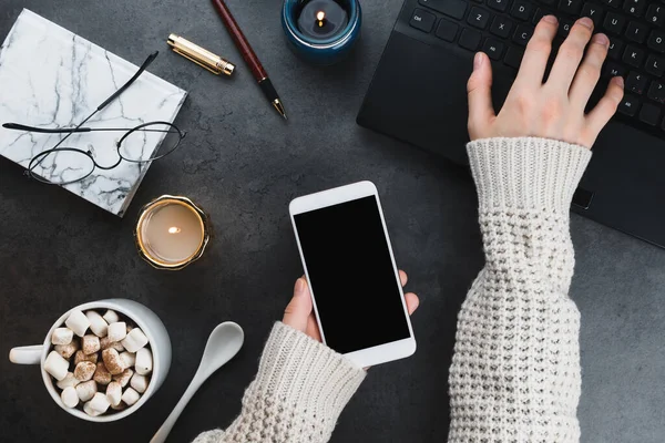 Cozy winter business flatlay arrangement with black laptop, women hands with vegan cocoa and candles on dark marble background