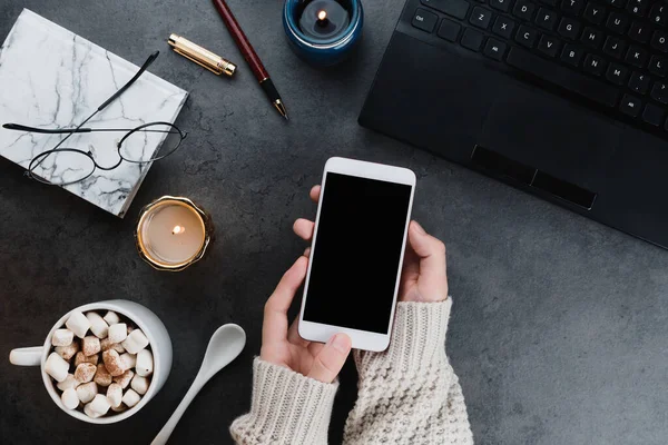 Cozy winter business flatlay arrangement with black laptop, women hands with vegan cocoa and candles on dark marble background