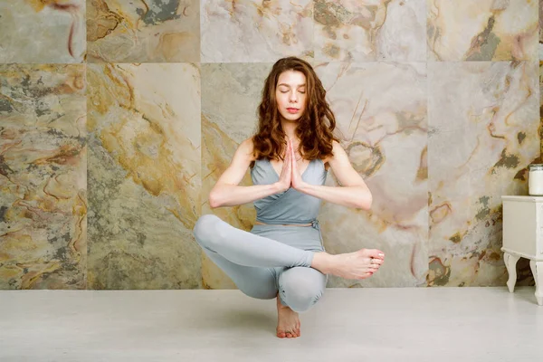 Young female practicing Toe Stand (Padangusthasana) Pose indoors, selective focus