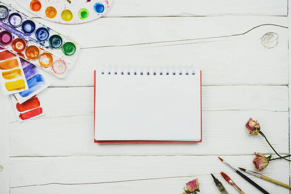 Плоская закладка блокнота на деревянном столе с палитрой, акварелью и другими канцелярскими принадлежностями
