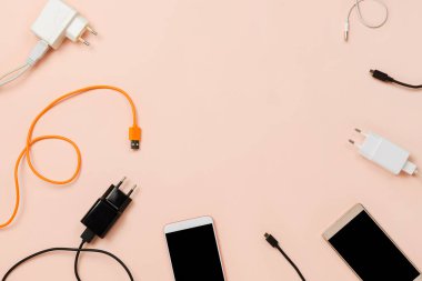 Pastel arka planda çeşitli fişler, kablolar ve akıllı telefonlar. Düz çerçeve, teknoloji veya bağlantı konsepti, telif alanı