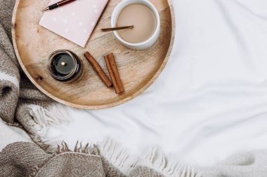 Ahşap tepsiyle, bir fincan kahveyle, kakaoyla, mumla, defterlerle beyaz çarşaflarla, battaniyelerle.