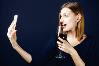 Genç bir kadın elinde bir bardak kırmızı şarapla selfie çekiyor.