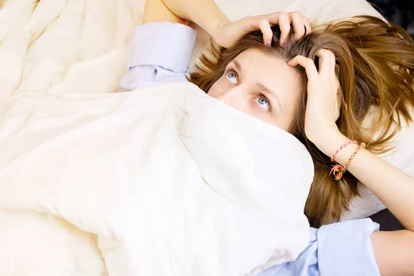 Young girl lying in her bed, face covered by blanket with eyes wide open with surprise. Selective focus, morning or night sleep concept.