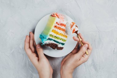 Gri arka planda, kadınların elinde düz bir gökkuşağı vejetaryen pastası.