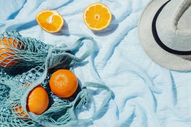 Portakalların piknik malzemesi mavi battaniyenin üzerinde bir eko torba ve şapka.