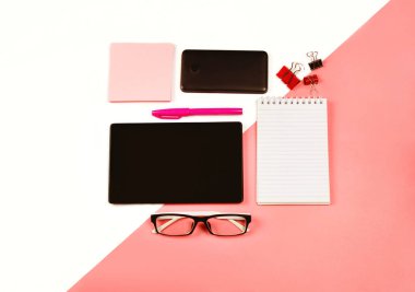 Siyah tabletli, defterli, telefonlu, gözlüklü, kağıt notlu, ataçlı ve kalemli bir kadın işyeri. Ofis aletleri. Pastel pembe ve beyaz. Düz yatıyordu.