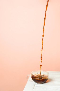 Beyaz bir masada cam bir fincana koyu kahve dökülüyor. Seçici odaklanma. Minimalist hareketsiz hayat