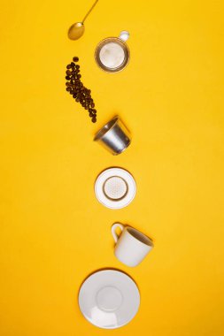 Kahve çekirdekleri parçalanmış Vietnam Phin kahve filtresinin içine düşüyorlar altın çay kaşığından çay fincanına ve çay tabağıyla birlikte beyaz espresso kahve bardağına. Düz çizgi, sarı arkaplan