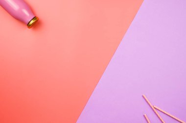 Bir tarafında meyve suyu ya da smoothie şişesi, diğer tarafında da kağıt kamış olan düz bir yatak. Sağlıklı gıda konsepti. Pembe ve mor arkaplan.