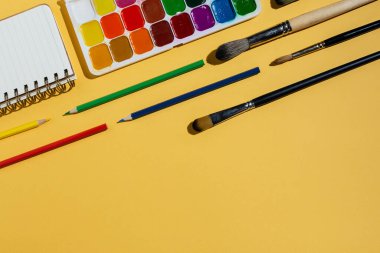 Suluboya, fırça, defter ve sarı üzerine diğer kırtasiye ve sanat malzemelerinin düz tablosu