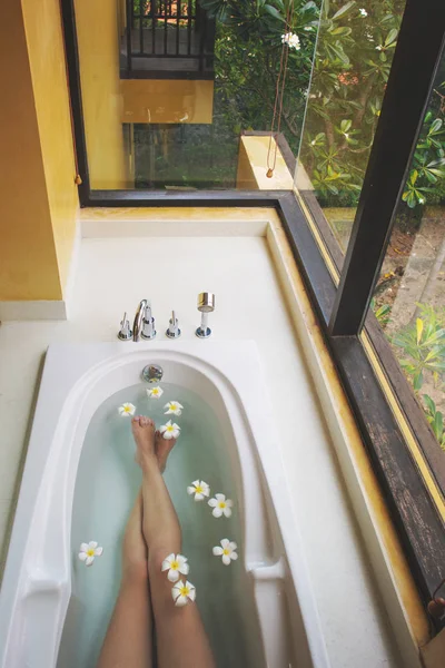 Frauenbeine in Badewanne mit Blumen — Stockfoto