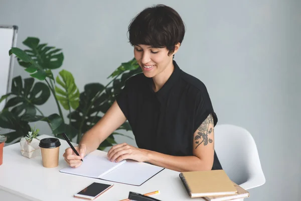 Geschäftsfrau sitzt am Schreibtisch und macht sich Notizen — Stockfoto