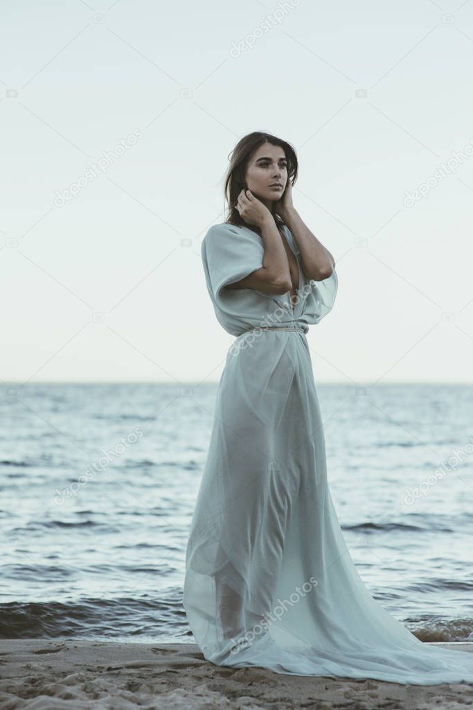 Beautiful woman in long white flowing dress standing on the beach