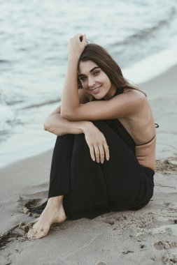 Gülümseyen gün batımında sahilde oturan kadın