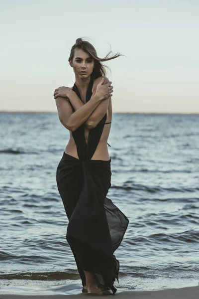 Hermosa chica en un vestido negro en la playa. —  Fotos de Stock