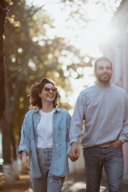 Sokakta yürürken el ele tutuşan ve gülümseyen genç çift.