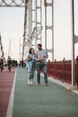 Tatlı gülümseyen çift pizza ve soğuk içecekler ile Köprü üzerinde yürüyen