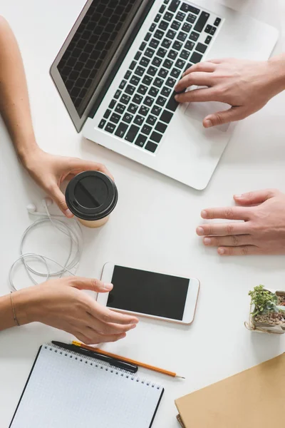 Blick von oben auf die Hände von Büroangestellten mit Laptop, Smartphone und Coffee to go lizenzfreie Stockfotos