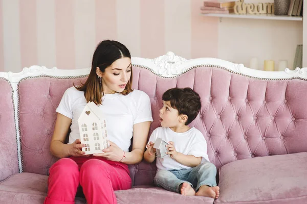 Ευτυχισμένη μητέρα και μικρός γιος κάθονται στον καναπέ και παίζουν με τα παιχνίδια σπίτια, ευτυχισμένο χρόνο και συντροφικότητα — Φωτογραφία Αρχείου