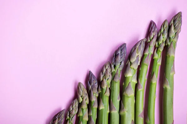 Groene verse asperges in rij op roze achtergrond — Stockfoto