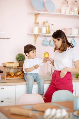 Küçük çocuk masada oturuyor ve annesinin elinden sarı armut. .