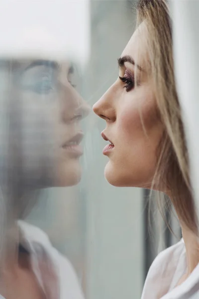 Vacker kvinna tittar på hennes reflektion i fönstret. — Stockfoto