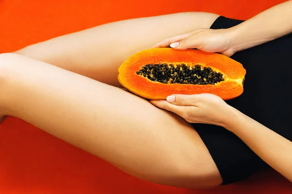 Vista recortada de la mujer sosteniendo la mitad de la papaya fresca en sus piernas sobre fondo naranja. Vista superior . —  Fotos de Stock