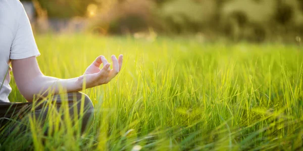 O homem está meditando na grama verde no parque no dia ensolarado de verão. Conceito de meditação e estilo de vida saudável — Fotografia de Stock