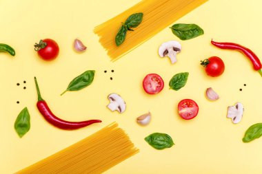 Sarı arka plan üzerinde domates, mürnküf, acı biber, fesleğen ve sarımsak ile Makarna